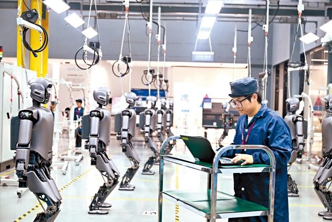 Acelerar a autossuficiência em ciência e tecnologia de ponta e liderar o desenvolvimento de novas forças produtivas é um foco fundamental do 15º Plano Quinquenal. A imagem mostra trabalhadores inspecionando um robô humanoide de uso industrial.